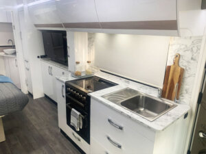 Compact campervan kitchen featuring modern appliances, sink, and marble countertop, optimized for space-saving cooking solutions.