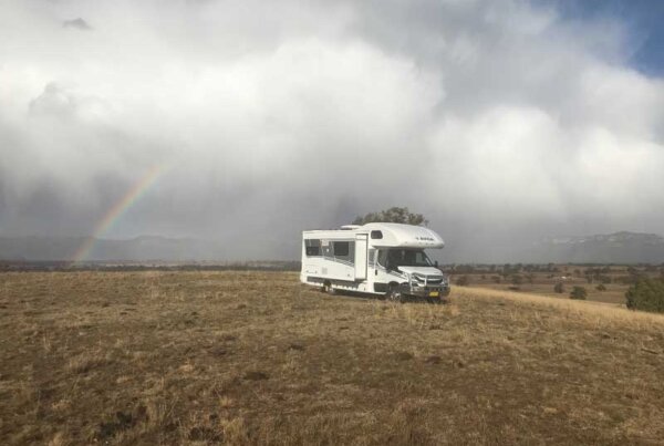Motorhome parked on a grassy hillside with a rainbow in the background, symbolizing adventure and exploration in Australia.