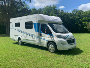 Avida motorhome parked on green grass, showcasing its sleek exterior design with blue accents, emphasizing maintenance and travel readiness for summer adventures.