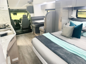 Interior of an Avida motorhome featuring a cozy bedroom with decorative pillows, a functional kitchen area with countertop, and a living space with a dining table, showcasing efficient use of space and modern design elements.