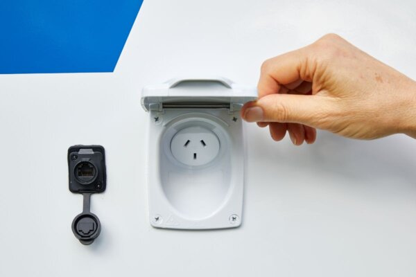 Hand opening the power inlet cover on the Avida Bruny motorhome, showcasing electrical connections for solar power and charging, emphasizing practical features for touring.