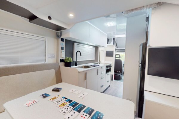 Interior view of Avida Bruny motorhome showcasing spacious living area with table and playing cards, modern kitchen, and comfortable lounge, emphasizing functionality and relaxation for travelers.