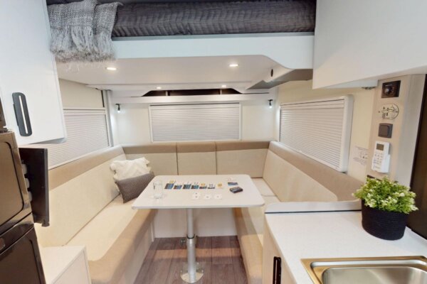 Interior view of Avida Bruny motorhome showcasing spacious rear lounge with drop-down bed, modern kitchen area, and dining table, emphasizing comfort and functionality for couples or small families.