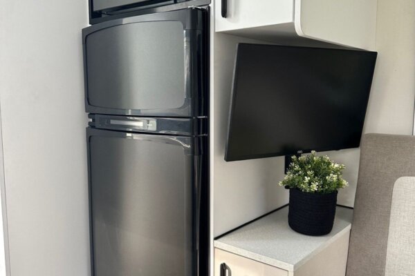 Interior view of Avida Bruny motorhome featuring a sleek black refrigerator and a mounted TV, highlighting the modern and functional design ideal for comfortable touring.