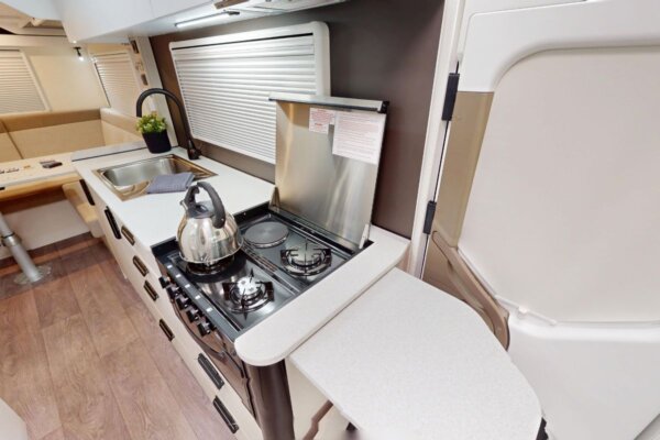 Avida Bruny motorhome kitchen interior featuring a well-equipped cooking area with a gas stove, kettle, and fold-down bench extension, designed for practical and spacious living on the road.