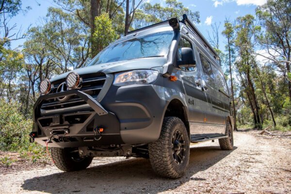 Avida Explorer LX 4x4 campervan parked on a dirt road, showcasing rugged off-road features, including a front bull bar, driving lights, and all-terrain tires, surrounded by lush greenery.
