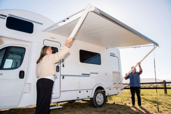 Couple extending an electric awning on Avida Silverton motorhome, showcasing outdoor living features and practical design.