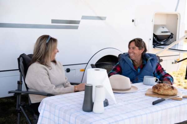 Couple enjoying coffee and bread at a table outside the Avida Silverton motorhome, showcasing outdoor living and comfort features.