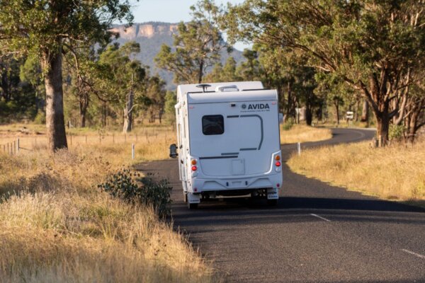 Avida Silverton motorhome driving on a winding road surrounded by trees and grasslands, showcasing its sleek design and outdoor adventure capabilities.