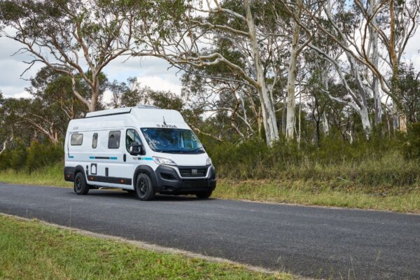 Avida Trek campervan driving on a scenic road surrounded by trees, showcasing its compact design and suitability for adventure travel.