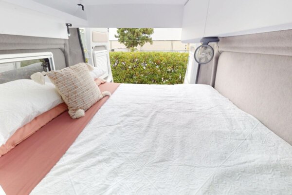 Avida Trek campervan interior showcasing a cozy fixed bed with decorative pillows, light bedding, and a compact design optimized for comfort and functionality.