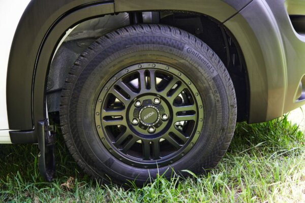 Avida Trek campervan wheel with black alloy rim and Continental tire, set against grassy background, highlighting the vehicle's robust design and off-road capability.