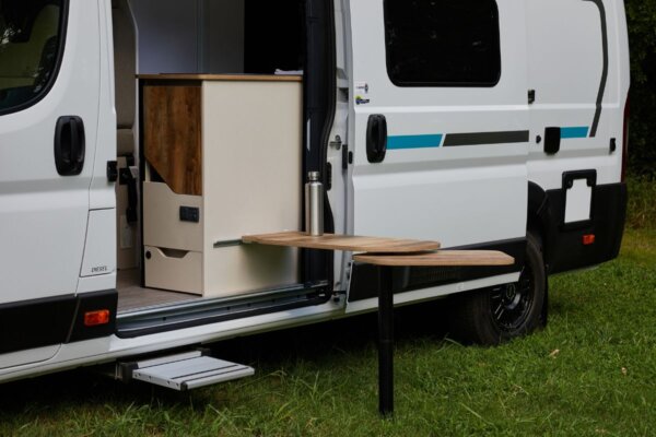 Avida Trek campervan exterior featuring a compact kitchen area with a foldable table, showcasing smart storage solutions and a streamlined design for outdoor dining.