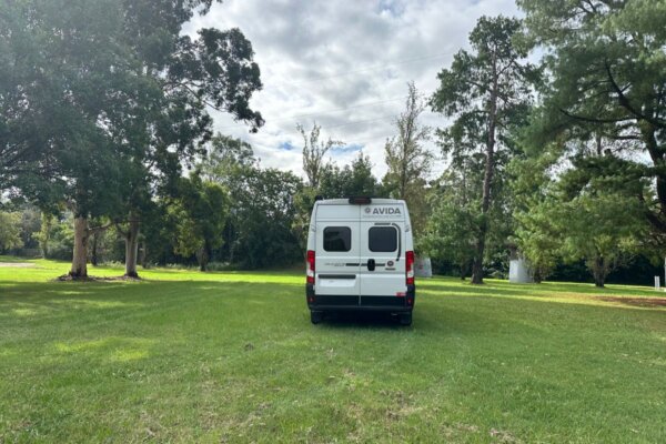 Avida Trek campervan parked on a grassy field surrounded by trees, showcasing its compact design and outdoor versatility.