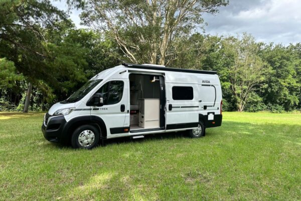 Avida Trek campervan parked in a grassy area, showcasing its open door and compact design, emphasizing outdoor adventure and practical living for travelers.