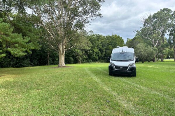 Avida Trek campervan parked on grassy field surrounded by trees, showcasing its compact design and outdoor versatility.