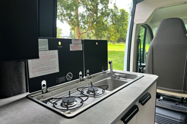 Compact campervan kitchen with dual gas burners, sink, and storage, showcasing Avida Trek's smart interior design and functionality for adventure travel.